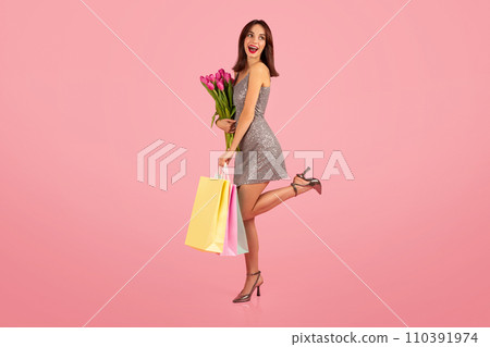 Cheerful young woman in a glittering dress joyfully holding a bouquet of pink tulips 110391974