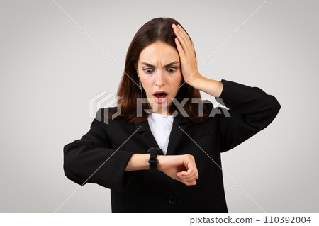 Shocked young European lady in suit, look at clock with open mouth Shocked young European lady in suit, look at clock with open mouth 110392004