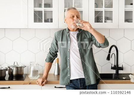 Healthy senior man drinking glass of water in his kitchen Healthy senior man drinking glass of water in his kitchen 110392146