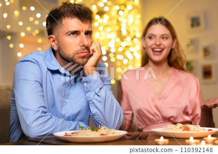 Pensive man at dinner, woman talking in festive setting 110392148