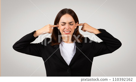 Sad tired young European woman in suit closed ears with hands, closed eyes Sad tired young European woman in suit closed ears with hands, closed eyes 110392162