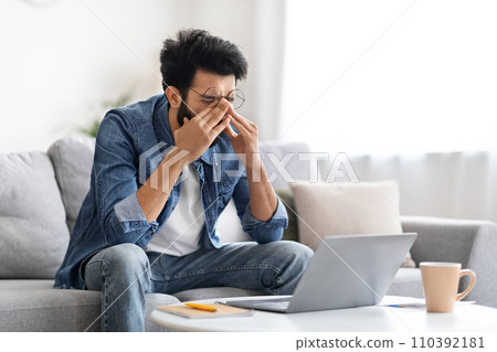 Tired indian man rubbing eyes, suffering fatigue while working on laptop Tired indian man rubbing eyes, suffering fatigue while working on laptop 110392181