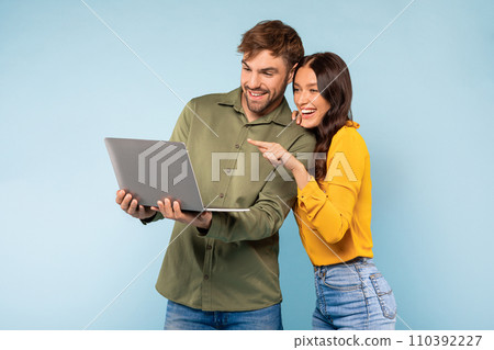 Couple with laptop smiling and pointing at screen on blue background 110392227