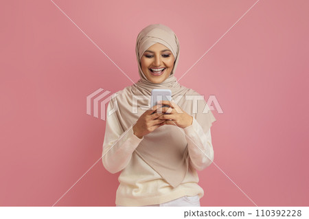 Cheerful arab muslim woman in hijab messaging on smartphone 110392228