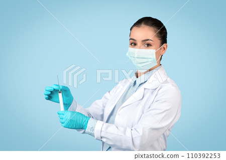 Focused woman doctor with syringe, protective gear on Focused woman doctor with syringe, protective gear on 110392253