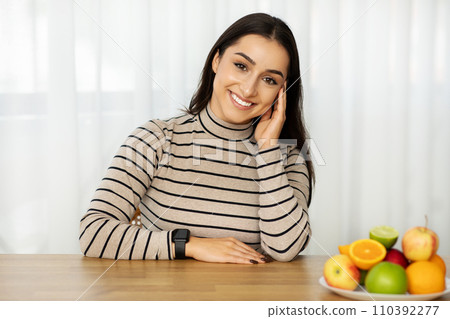 Cheerful young caucasian woman with smartwatch leans on hand, smiling at camera Cheerful young caucasian woman with smartwatch leans on hand, smiling at camera 110392277