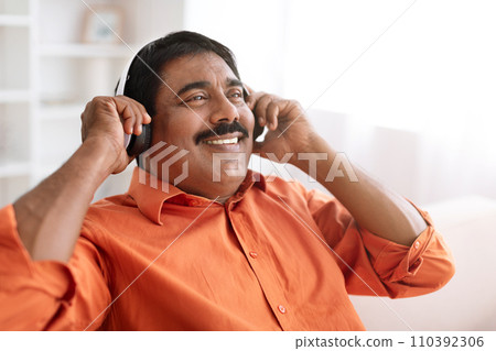 Closeup of middle aged indian man using wireless headphones Closeup of middle aged indian man using wireless headphones 110392306