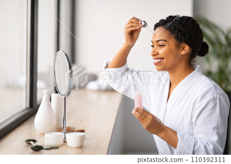 Skincare Concept. Beautiful Black Woman Applying Face Serum With Dropper Skincare Concept. Beautiful Black Woman Applying Face Serum With Dropper 110392311