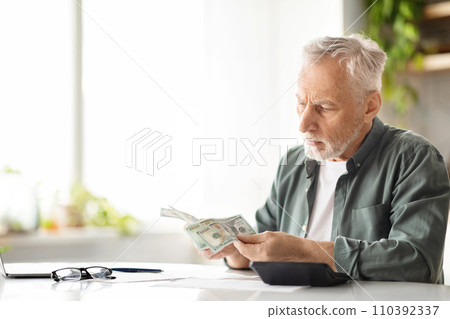Senior male counting dollar cash while sitting at table in kitchen 110392337