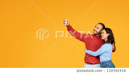 Romantic casual spouses take selfie on smartphone, orange background Romantic casual spouses take selfie on smartphone, orange background 110392416