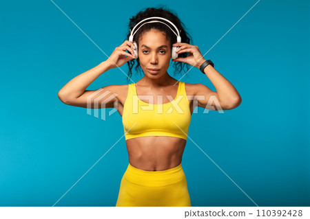 Fit black lady using wireless headphones while training in studio Fit black lady using wireless headphones while training in studio 110392428