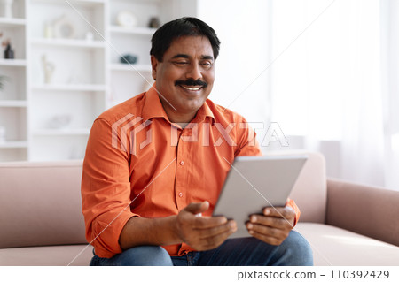 Positive indian man using digital tablet at home Positive indian man using digital tablet at home 110392429