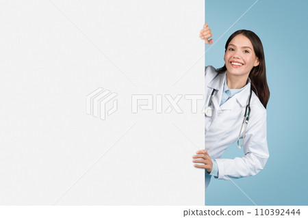 Smiling young woman doctor peeking from behind banner 110392444