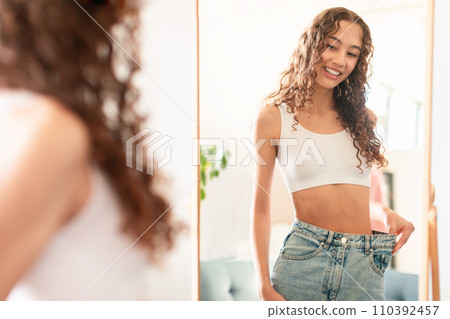 Caucasian teen girl compares size at home, wearing big jeans 110392457