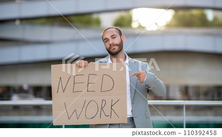 Young man holding 'Need Work' sign, illustrating the search for employment opportunities 110392458