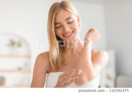 Attractive blonde woman applies moisturizer on elbow in bathroom Attractive blonde woman applies moisturizer on elbow in bathroom 110392475
