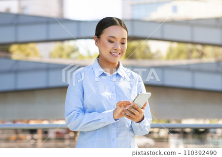 Happy Asian entrepreneur woman using smartphone app outside office building Happy Asian entrepreneur woman using smartphone app outside office building 110392490
