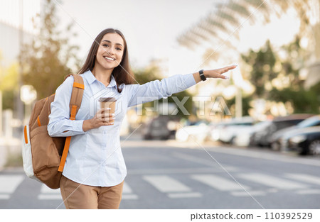 A smiling young woman in a casual button-down shirt and khaki pants, holding a coffee cup 110392529