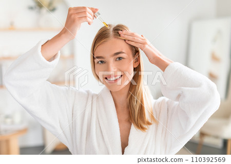 Joyful woman treats hair roots applying nourishing serum in bathroom Joyful woman treats hair roots applying nourishing serum in bathroom 110392569