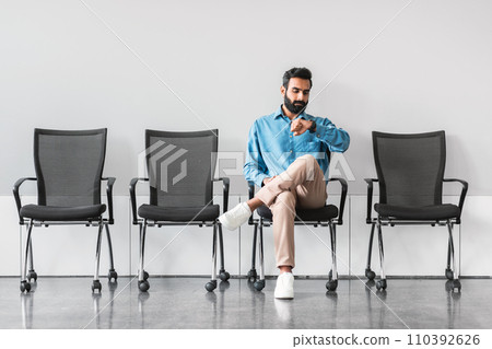 Indian man checking time while waiting in a row of chairs 110392626
