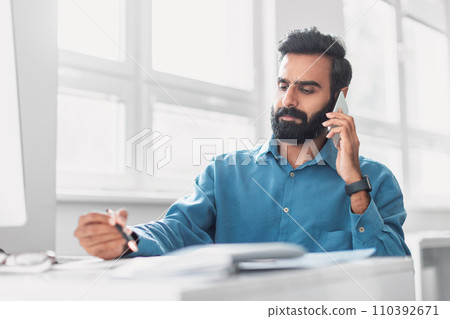 Serious indian businessman on phone call while reviewing documents 110392671