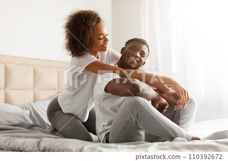 Loving Black Woman Hugging Her Husband Sitting On Bed Indoor 110392672