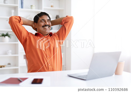 Cheerful dreamy mature indian man sitting at home office 110392686