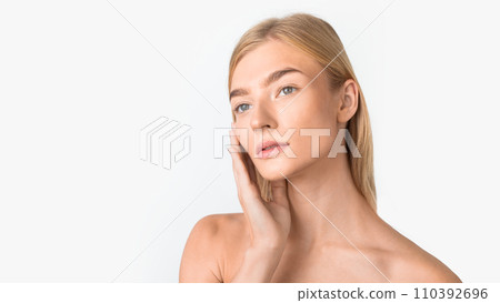 Gorgeous blonde lady touching her soft skin on cheek, studio 110392696