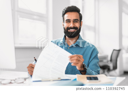 Smiling indian businessman holding paperwork, office setting Smiling indian businessman holding paperwork, office setting 110392745