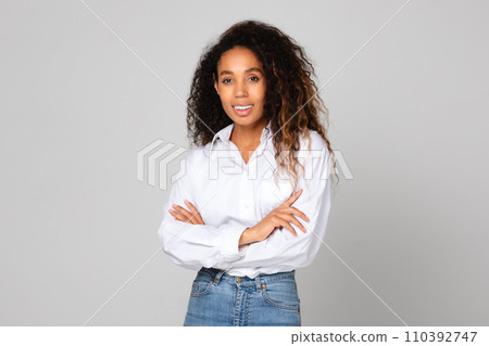 Black young lady crosses hands standing with confidence, gray backdrop 110392747