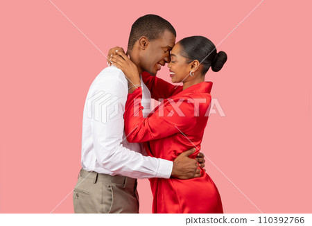 Intimate african american couple in loving embrace on soft pink backdrop Intimate african american couple in loving embrace on soft pink backdrop 110392766