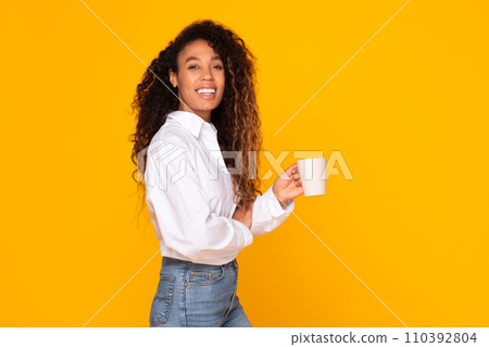 Happy African American woman holding coffee mug on yellow background 110392804