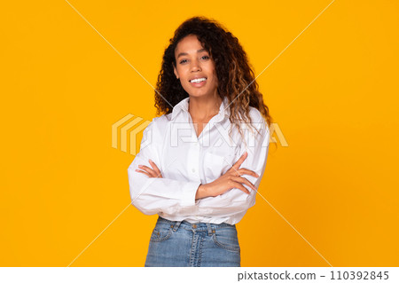 African American young woman poses crossing hands against yellow backdrop African American young woman poses crossing hands against yellow backdrop 110392845