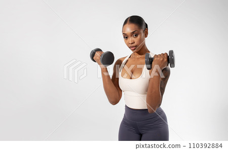 african american lady holds dumbbells works out against white backdrop 110392884