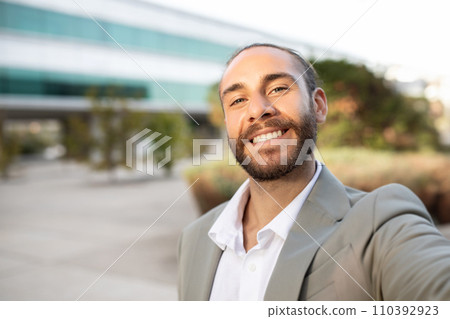 Friendly handsome young businessman in suit taking selfie outdoors 110392923