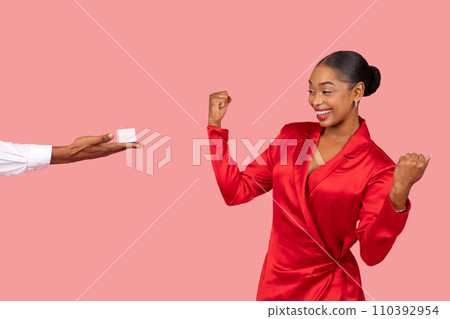 Excited black woman celebrating, man offering ring box on pink background 110392954