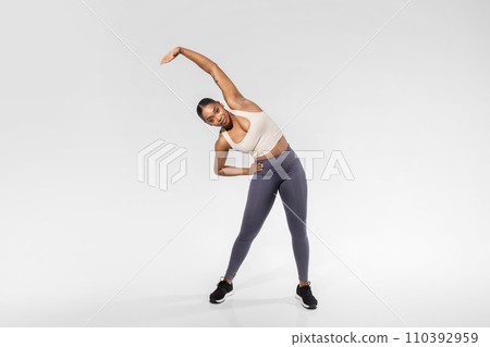 Black Lady Stretching Raised Arm While Bending Core, White Background 110392959