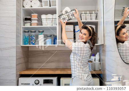 Woman organizing white bathroom laundry comfortable storage on cupboard shelves Woman organizing white bathroom laundry comfortable storage on cupboard shelves 110393057