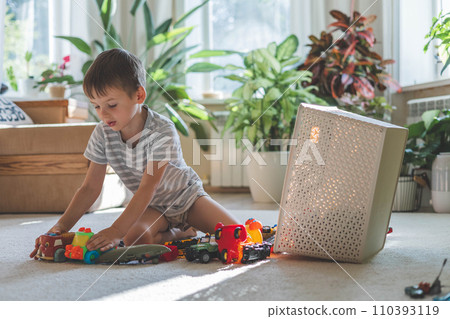A cheerful European boy plays with cars on the carpet in his room. A cheerful European boy plays with cars on the carpet in his room. 110393119