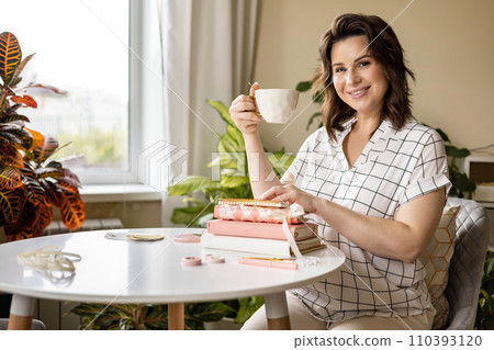 Smiling young business woman planning work making notes in paper diary at comfortable home 110393120