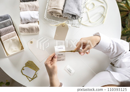 Woman hands cutting sticker tag scissors comfortable storage organizing linen textile in container Woman hands cutting sticker tag scissors comfortable storage organizing linen textile in container 110393125