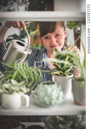 A young woman enjoys caring for flowers. Watering indoor plants and admiring them. A young woman enjoys caring for flowers. Watering indoor plants and admiring them. 110393155