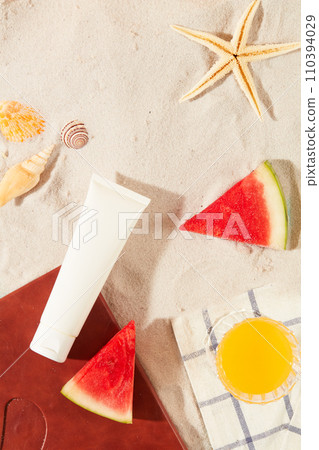 Flat lay of an unlabeled cosmetic tube with snail shells, starfish, watermelon and a glass of orange juice on a smooth sandy background. Cosmetic mockup for advertising. Flat lay of an unlabeled cosmetic tube with snail shells, starfish, watermelon and a glass of orange juice on a smooth sandy background. Cosmetic mockup for advertising. 110394029