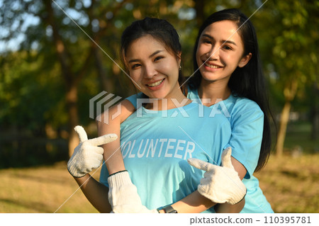 Two cheerful women pointing finger on volunteer title text on t-shirt while standing outdoor Two cheerful women pointing finger on volunteer title text on t-shirt while standing outdoor 110395781