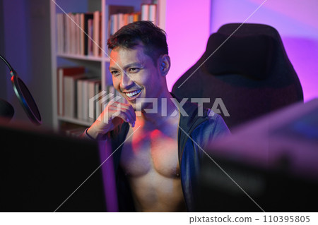 Confident muscled Asian male podcaster streaming audio podcast at home with neon lights Confident muscled Asian male podcaster streaming audio podcast at home with neon lights 110395805