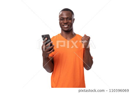 young african man dressed in orange t-shirt holding phone and chatting on social media young african man dressed in orange t-shirt holding phone and chatting on social media 110396069