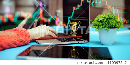 Close up of businesswoman using laptop computer and holding trophy cup on table with forex chart Close up of businesswoman using laptop computer and holding trophy cup on table with forex chart 110397242