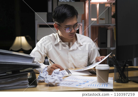 Young businessman working overtime on a desk at night.. Young businessman working overtime on a desk at night.. 110397259