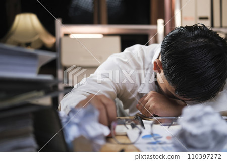 Young tired businessman lying on table at night office.. 110397272