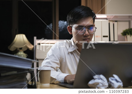 Young businessman working overtime on a desk at night.. 110397283